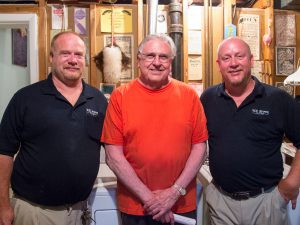 Three men standing next to each other smiling in a basement